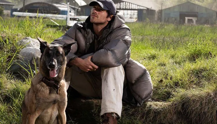 Hig, interprété par Jacob Elordi, assis dans l’herbe avec son chien près d’un aérodrome abandonné.